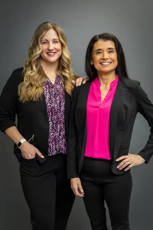 Two smiling people standing together in black jackets against a grey studio background