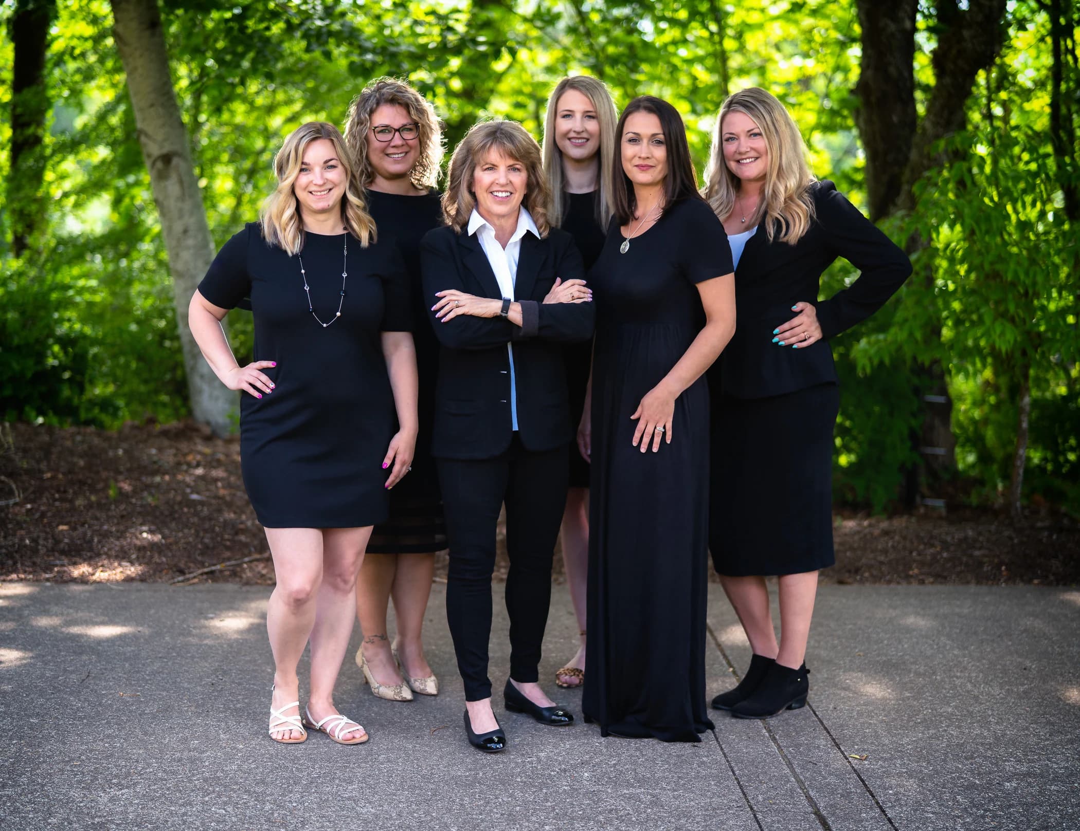 Six people in black outfits standing close together under trees
